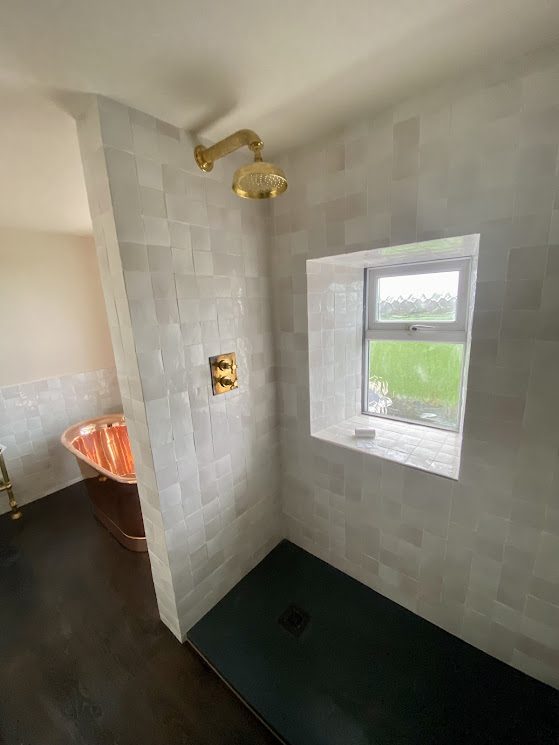 Tiled shower room with brass shower fittings and copper bath