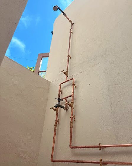 Outdoor shower with exposed copper pipework against a rendered wall